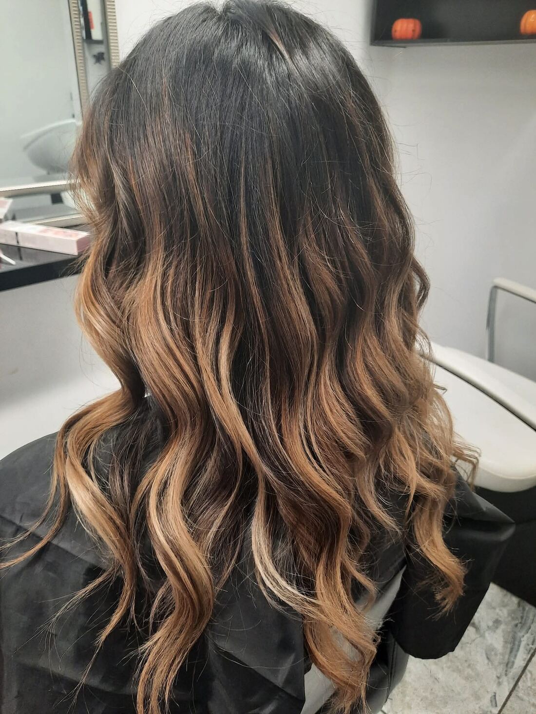 Loose waves on dark brown hair, with warm caramel balayage running through the mid-lengths and ends.